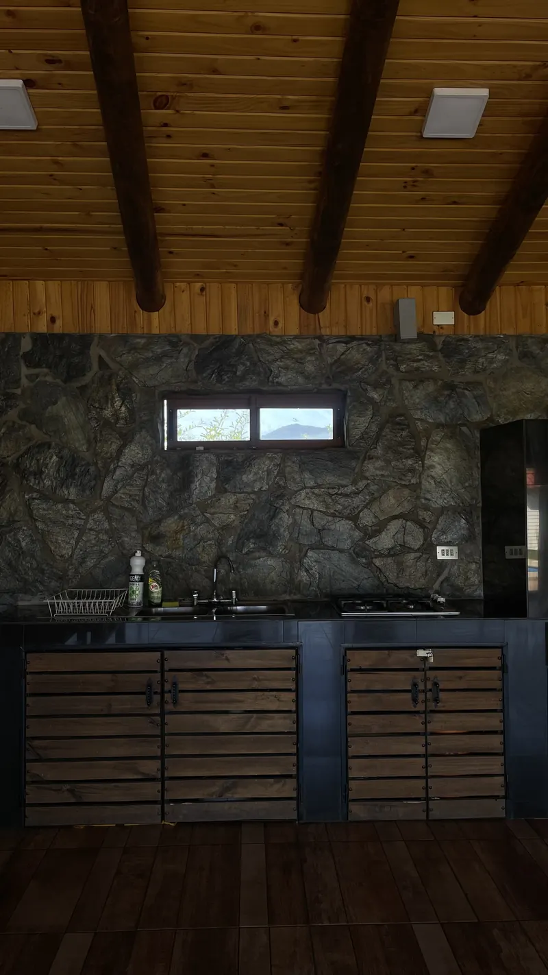 Cocina del quincho con encimera, lavaplatos y muro de piedra