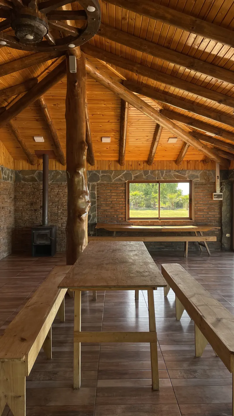 Mesón de madera con bancas dentro del quincho, junto a una ventana con vista al jardín