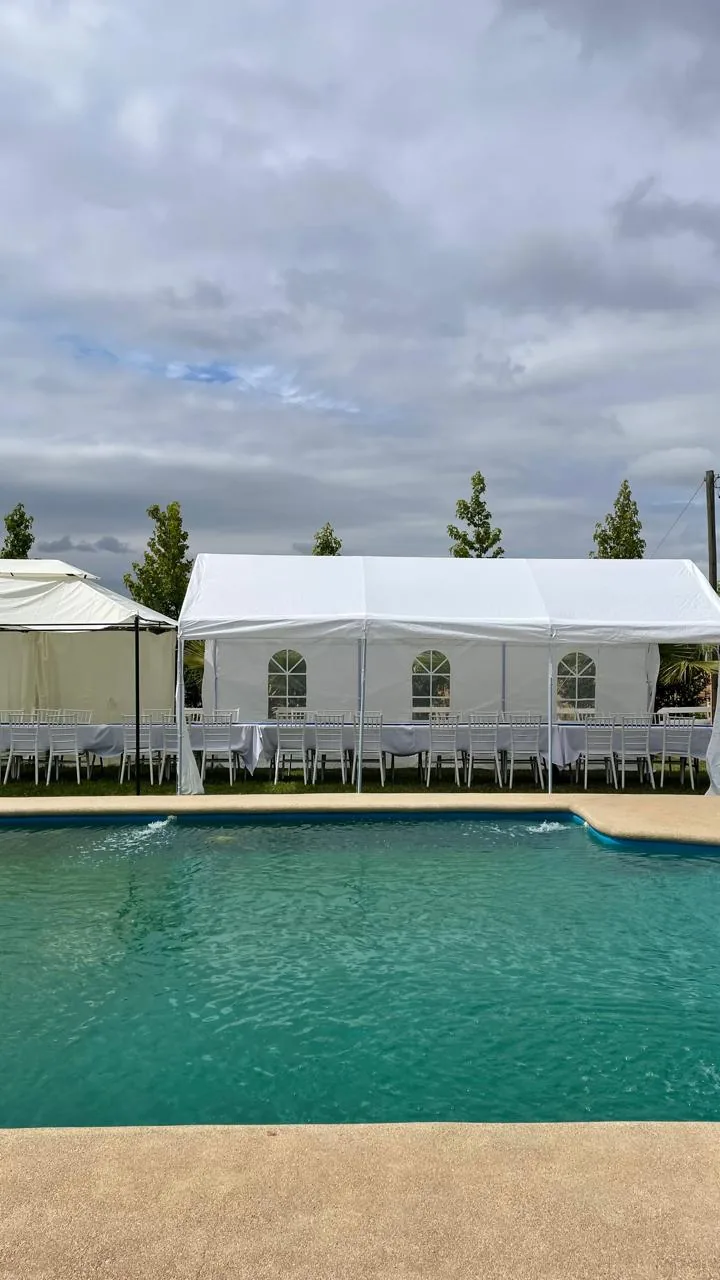 Toldos blancos con mesas y sillas montadas junto a la piscina
