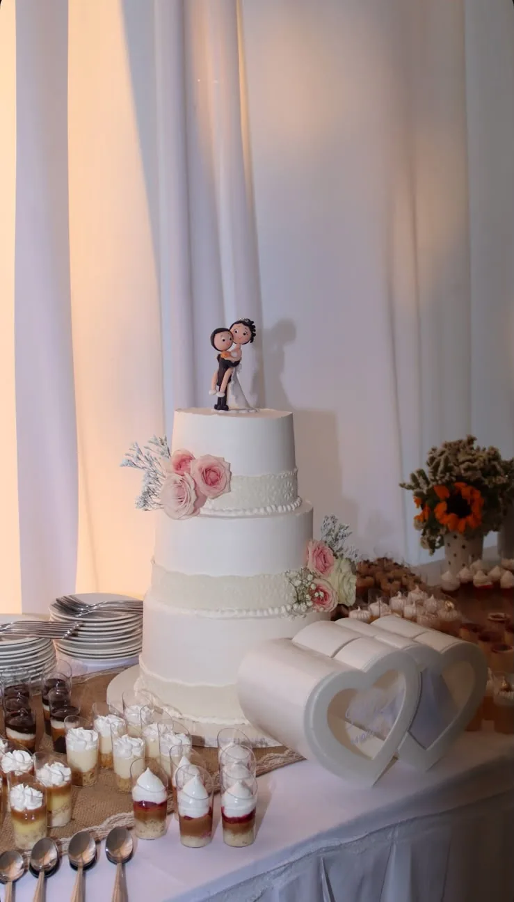 Torta de matrimonio de tres pisos con flores y mesa de postres en vasitos